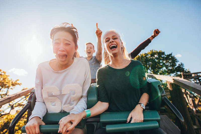 Enthusiastic young friends riding roller coaster ride at amusement park. Young people having fun at amusement park.