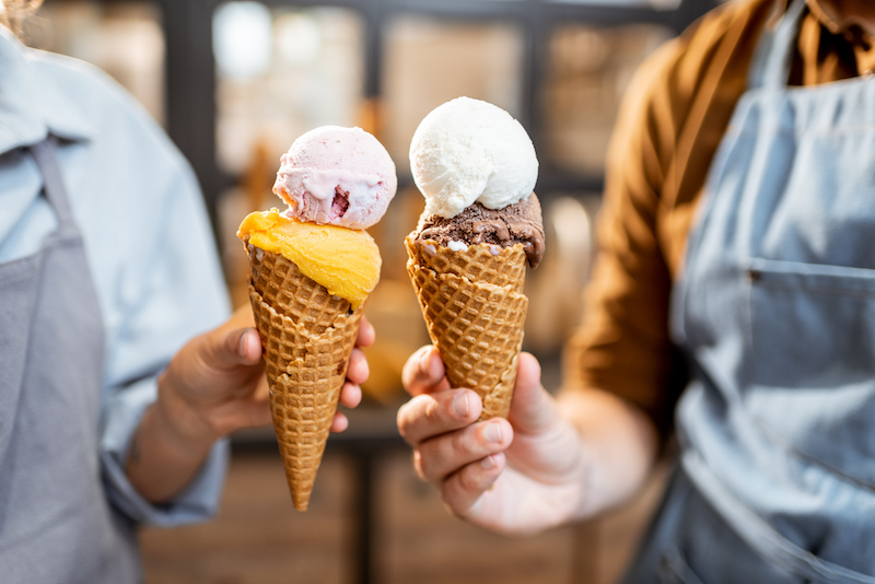 Two sellers cheering with yummy ice creams in waffle cone, having fun while selling ice cream at the shop, close-up