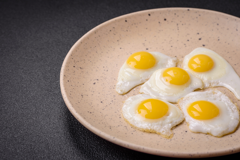 Delicious nutritious breakfast of fried quail eggs, bacon, legumes and cherry tomatoes with salt, spices and herbs on a dark concrete background