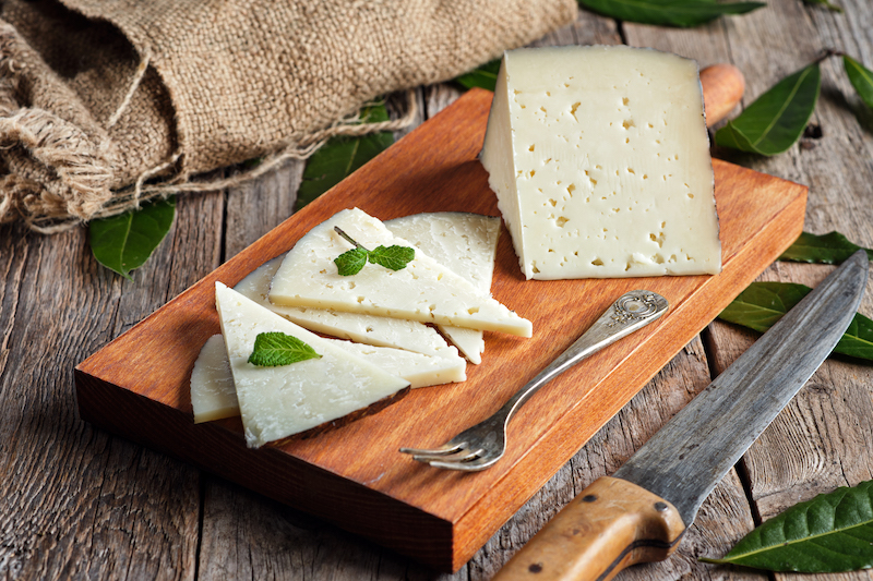 Slices of cured Manchego cheese on a wooden board with a rustic background