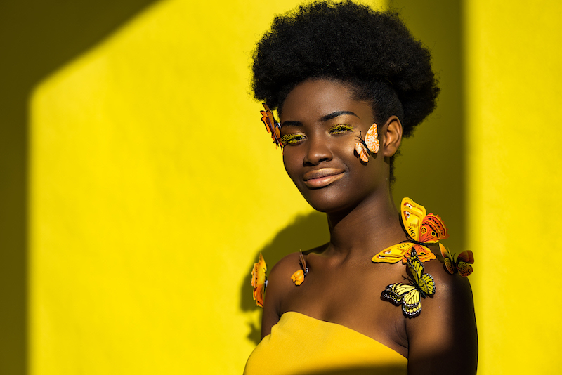Smiling pretty african american woman with butterflies on yellow