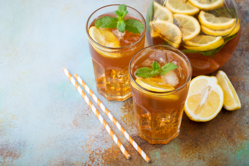 Traditional iced tea with lemon, mint and ice in tall glasses. Two glasses with cool summer drink on old rusty background.
