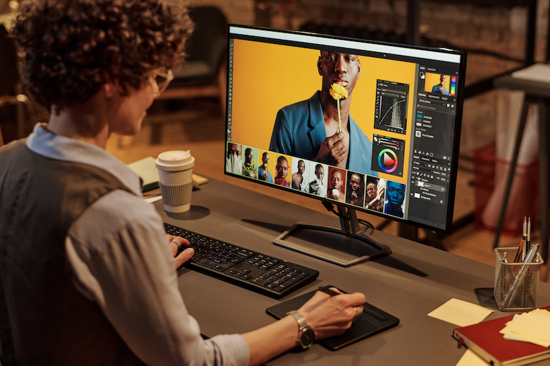 Rear view of woman using graphic tablet to edit photos on computer while sitting at her workplace at office