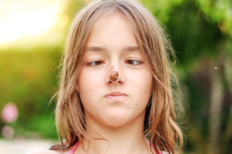 Funny preteen girl looking at snail on her nose. 