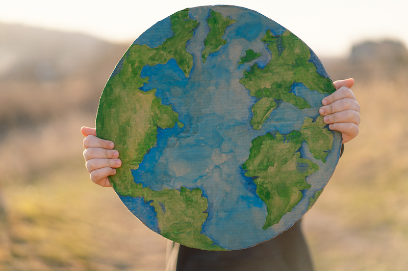  Little boy holding planet in hands against green spring background. 