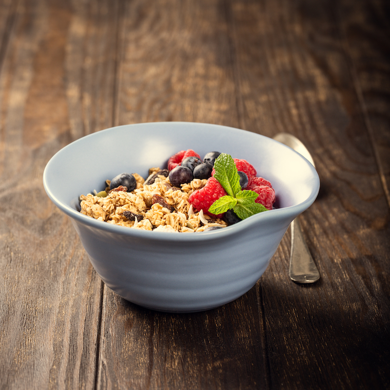 Oat granola with berries and yoghurt in blue bowl on dark old wooden background. 