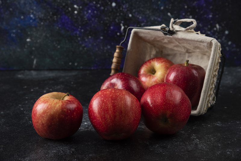 Ripe organic red apples out of basket on black background.