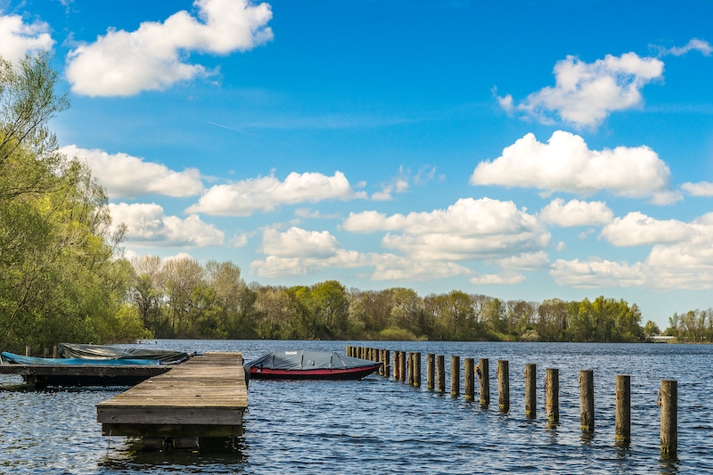 A sea with boats near the dock and green trees in the distance under a blue sky