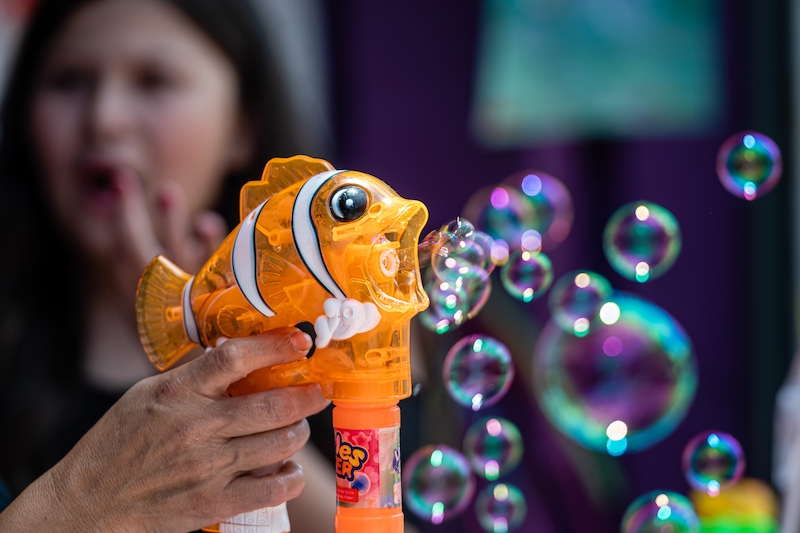  the toy seller is demonstrating to the buyers a soap bubble gun