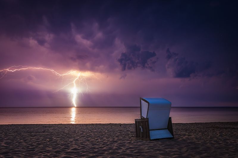 Dramatic lightning during a thunderstorm over the Baltic Sea with a beach chair on the shore