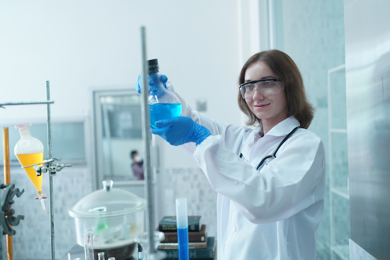 scientist in protective wear taking sample and examining it during experiment in the lab with his colleagues in the background