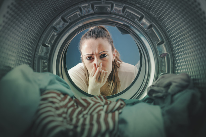 Woman staring at the laundry in the washing machine and holding her nose