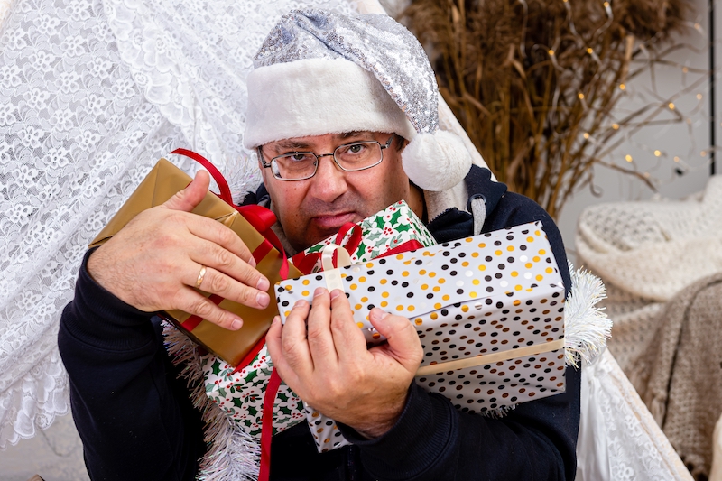 middle-aged man with glasses and a silver dwarf hat with Christmas gift boxes in a decorated room, Christmas concept