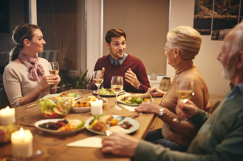 Young man and his wife communicating with his senior parents during family meal in dining room.