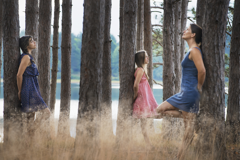 A group of people communing with nature, and leaning against tall straight trees in woodland.