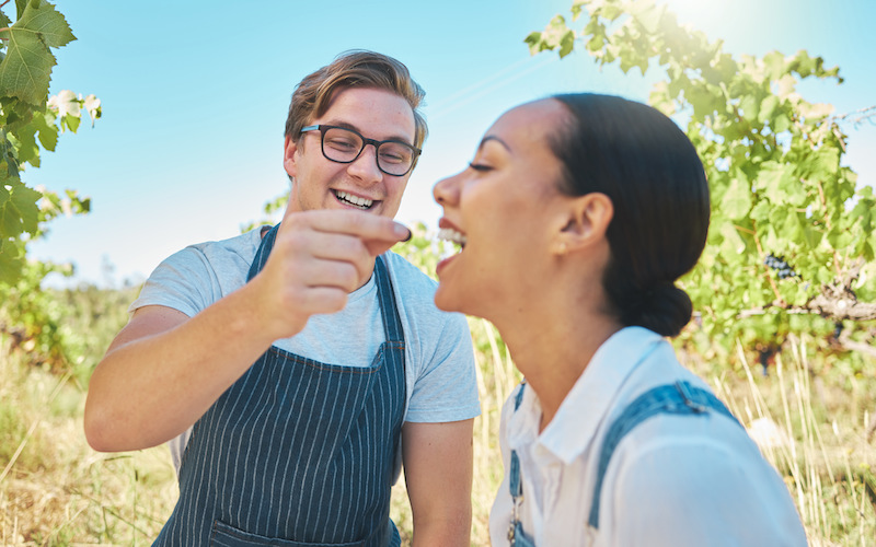 Love, agriculture and couple enjoying a happy moment sharing grapes on a wine tasting farm.