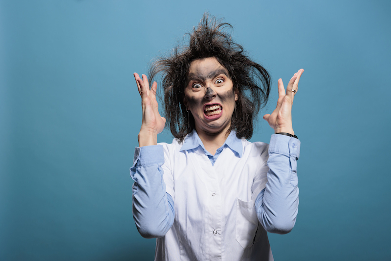 Mad biochemist with amusing look after laboratory explosion being angry while gesturing with rage. Goofy looking crazy scientist with dirty face and messy hair after failed chemical experiment.