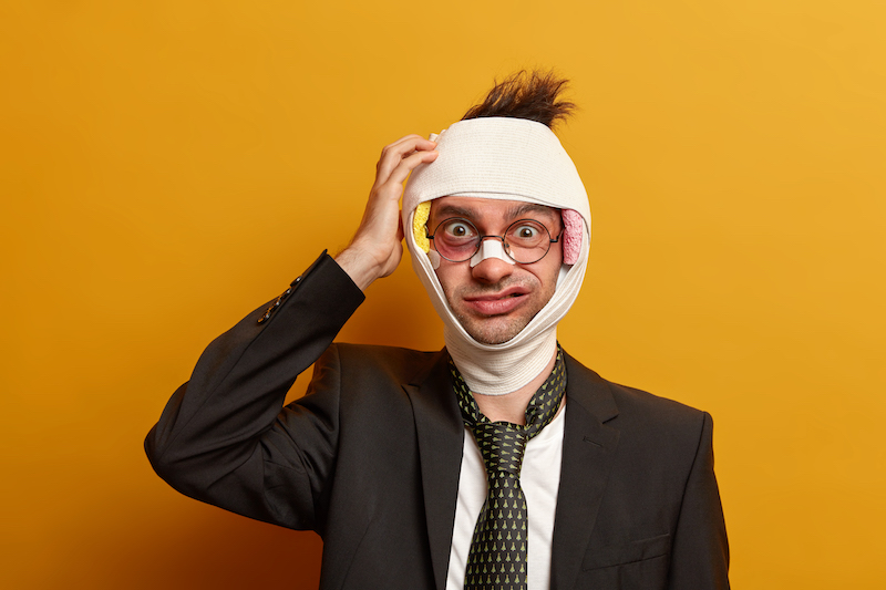 Photo of puzzled Caucasian man scratches head after brain concussion, feels unhappy, broken nose with adhesive plaster, shiner under eye, recovers for long period of time isolated on yellow background