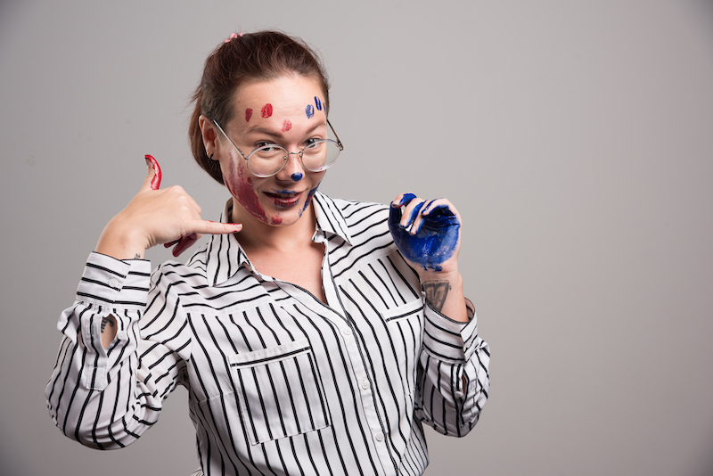 Woman with paints on her face and glasses on gray background