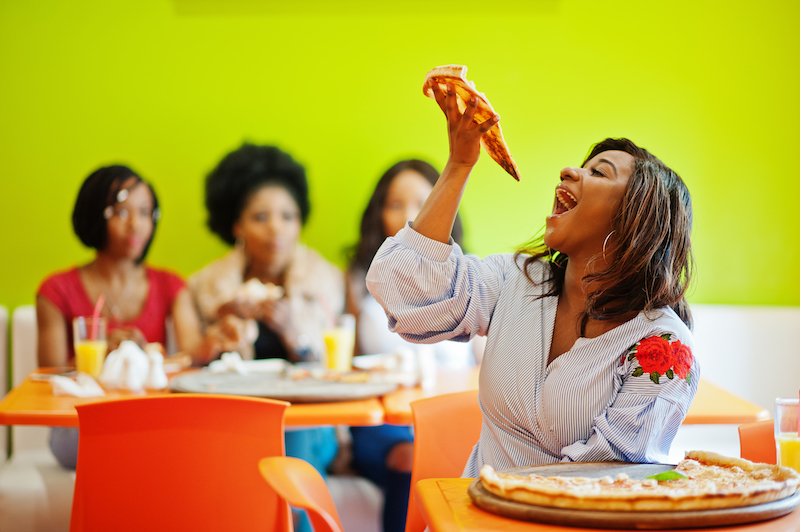 Woman holding up a slice of pizza sitting at restaurant