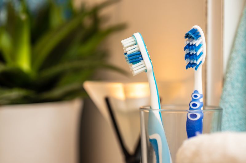 A closeup shot of two blue toothbrushes in a glass with towels