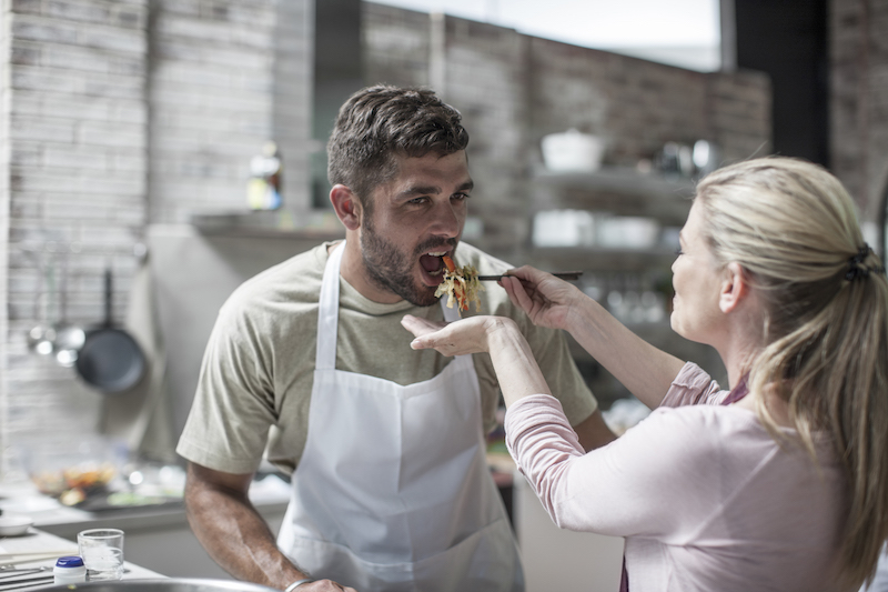 Couple cooking together and tasting food in kitchen