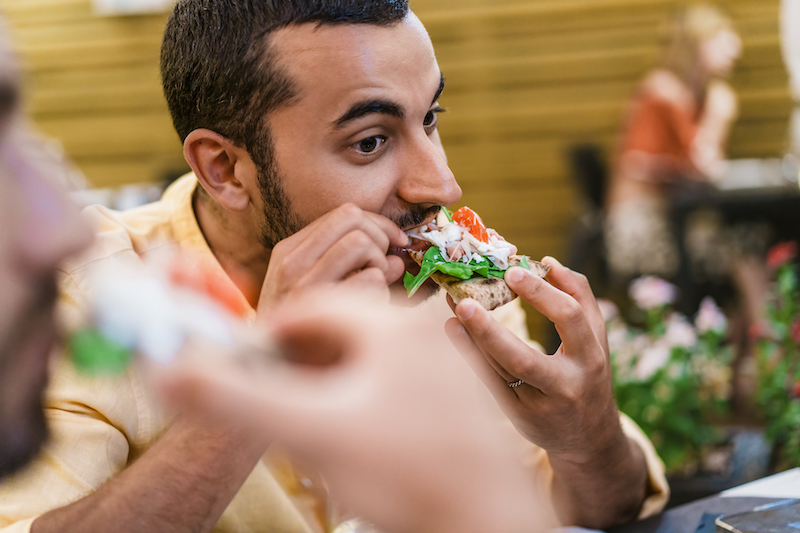 Close-up of young Italian man enjoying fresh slice of pizza in a casual cafe setting