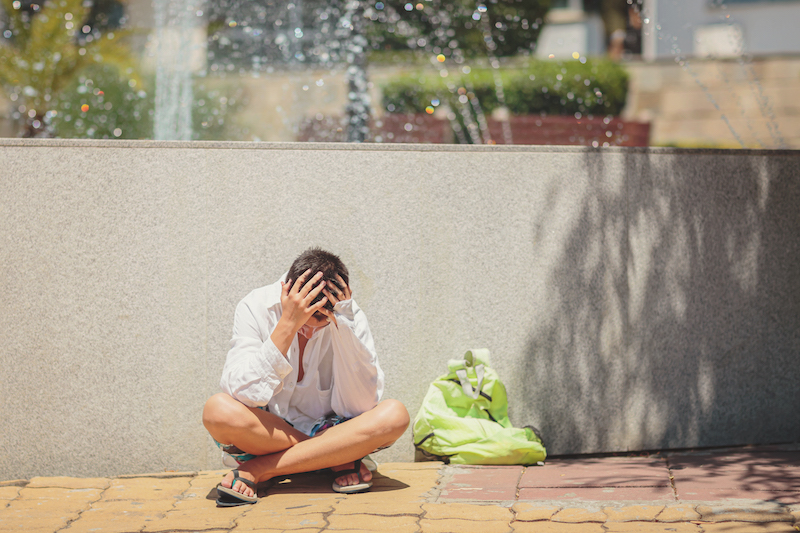 Sad depressed teenager sitting upset near the fountain and holding his head in his hands. The idea of protecting children and children's mental health