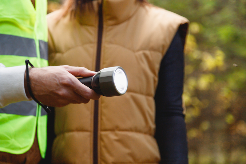 Search and rescue squad of volunteers with a flashlight in the forest, close-up on a flashlight in hand. 