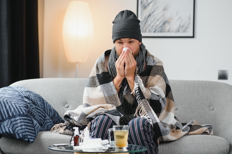 Sick man on sofa at home and blowing nose