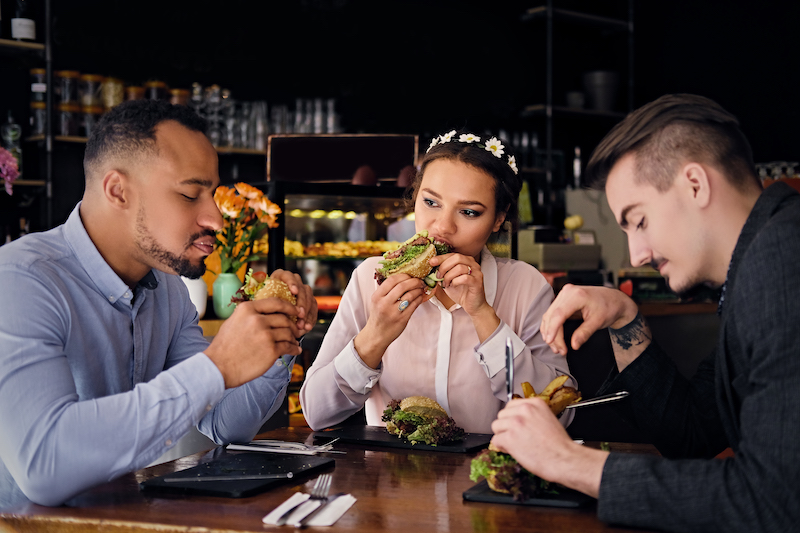 Three people eat vegetarian sandwiches in a cafe.