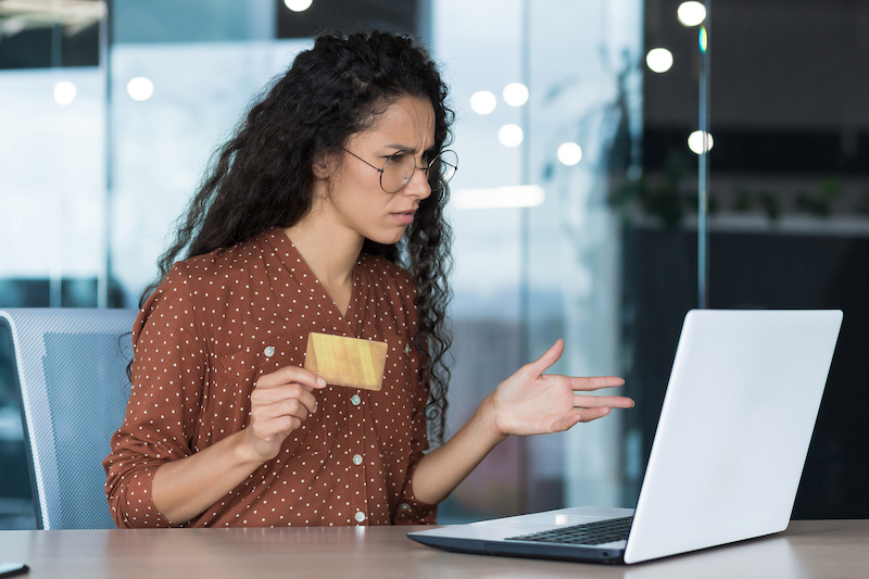 Upset and disappointed businesswoman working in modern office, using laptop and bank credit card to transfer money and shop online in online store, cheated evil employee