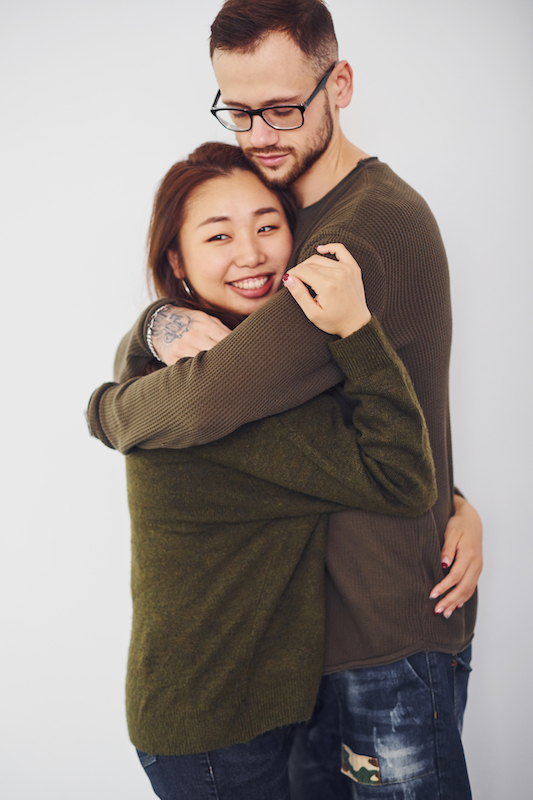 Happy multi ethnic couple in casual clothes embracing each other indoors in the studio. Caucasian guy with asian girlfriend.