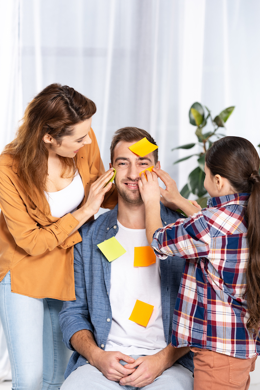 cheerful woman and kid putting yellow sticky notes on handsome man